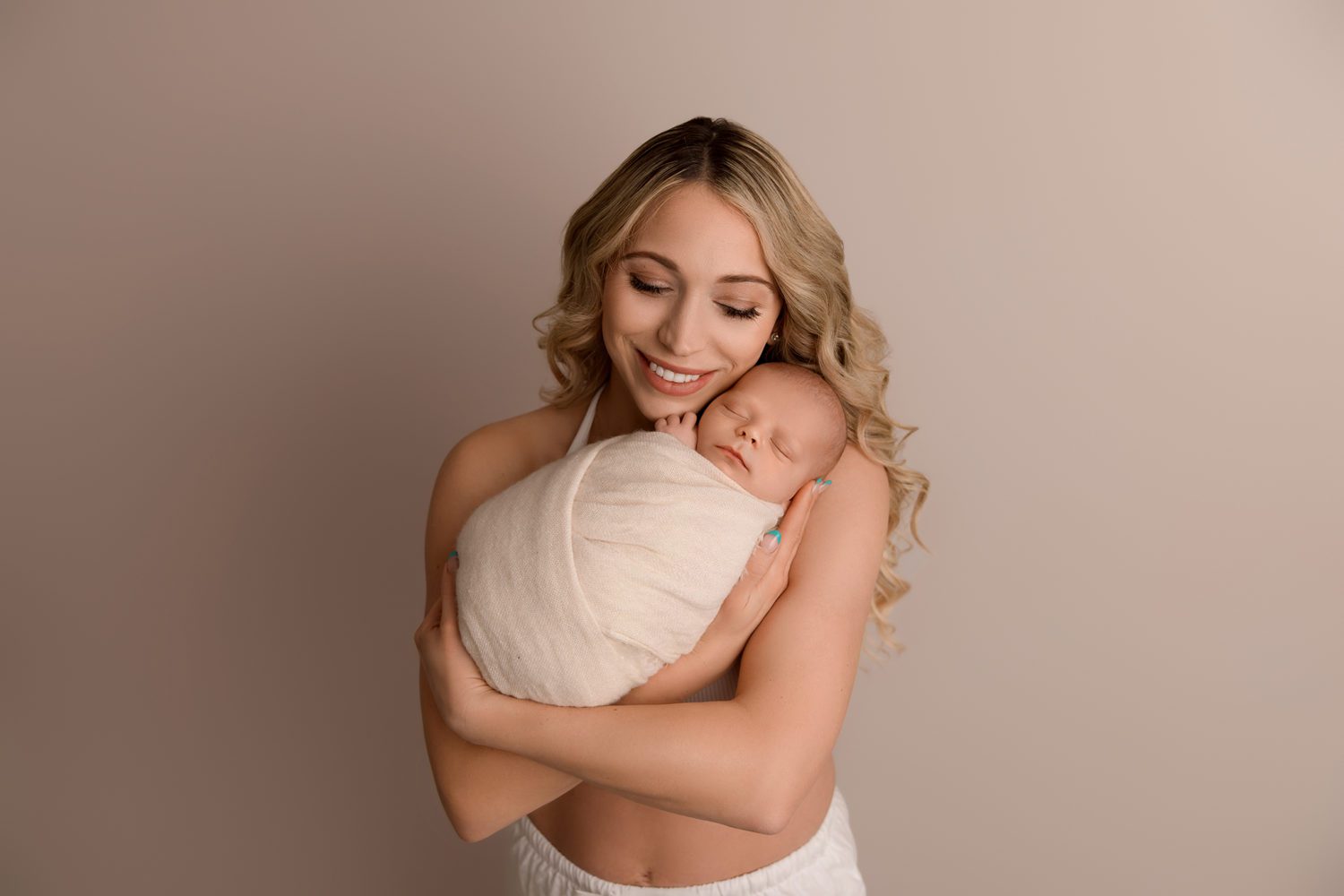 top 8 tips for a successful newborn session -newborn being held by mum on cream backdrop. mum smiling.