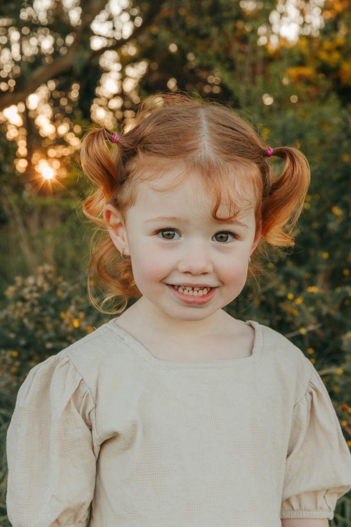 little girl. smiling cheekily at camera. red hair