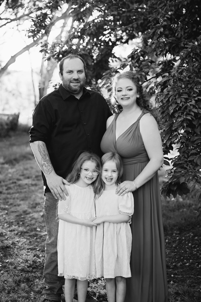 Greta Family photos. mum dad and two daughters standing together smiling at the camera. black and white photo