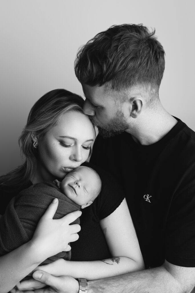 newborn photographer Perth Black and white intimate studio portrait of both parents with their newborn baby boy — newborn photography by Aurora Joy Photography, Stirling Western Australia