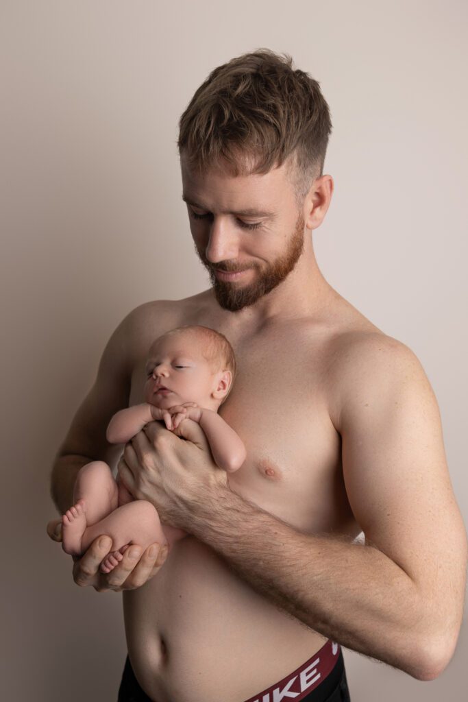 photo of a father holding his newborn baby boy in a backlit studio — newborn photography by Aurora Joy Photography, Stirling Western Australia