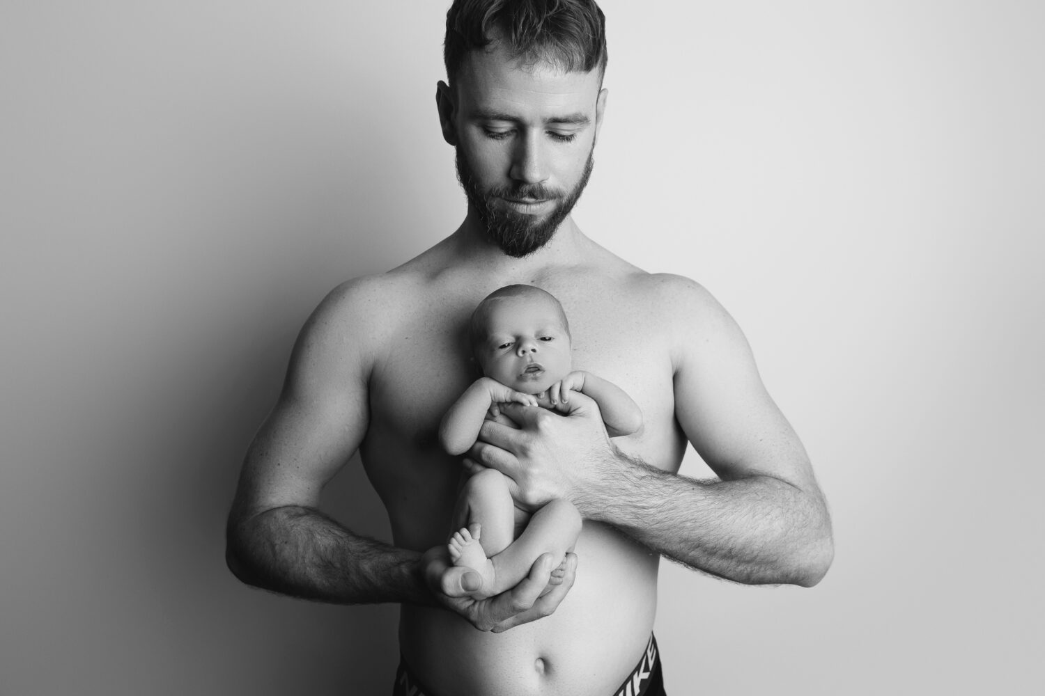 Black and white silhouette of a father holding his newborn baby boy in a backlit studio — newborn photography by Aurora Joy Photography, Stirling Western Australia